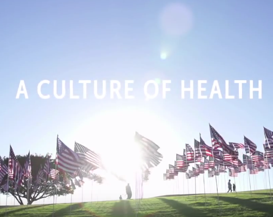 The words a culture of health displayed with an image of a grassy field and American flags